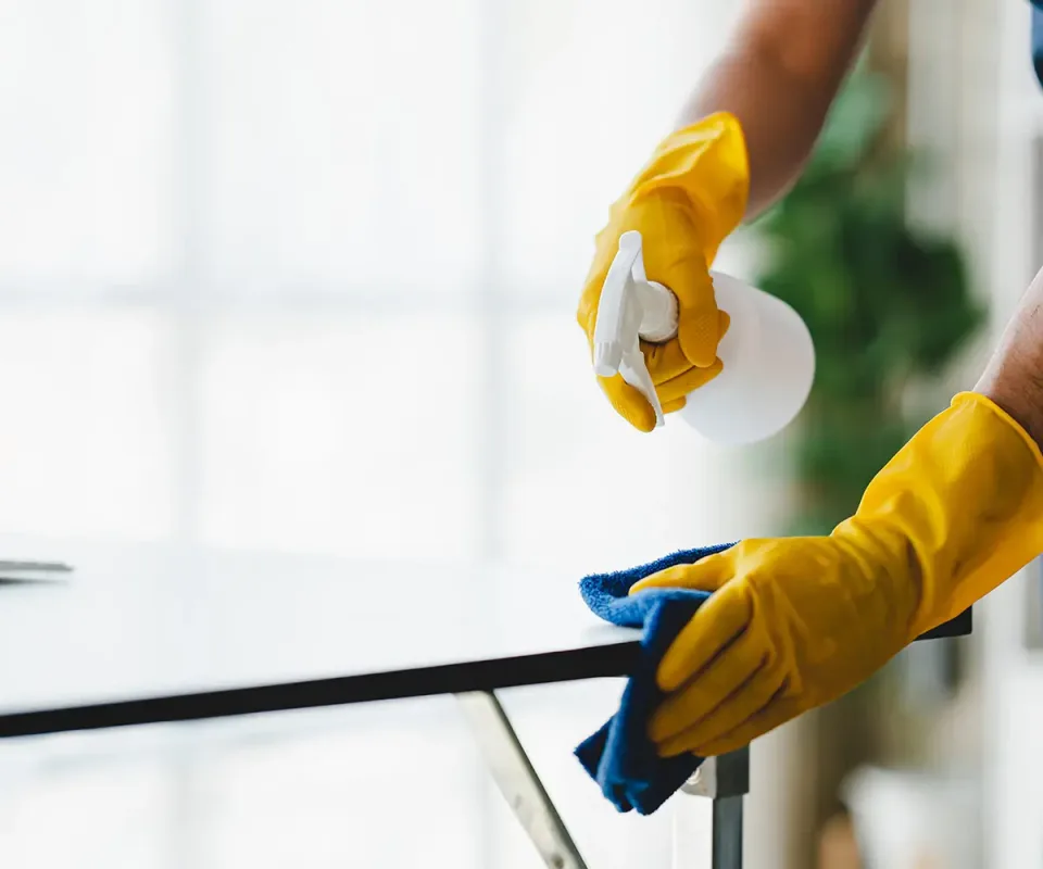 Gloved hands spraying and wiping down a glass surface with a cloth
